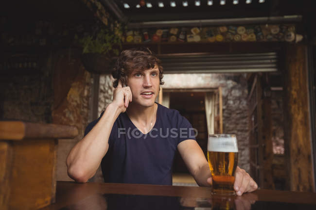 Чоловік говорить на мобільному телефоні в барі зі склянкою пива в руці — стокове фото