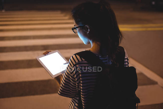 Vista trasera de la mujer joven usando tableta digital en la calle por la noche - foto de stock