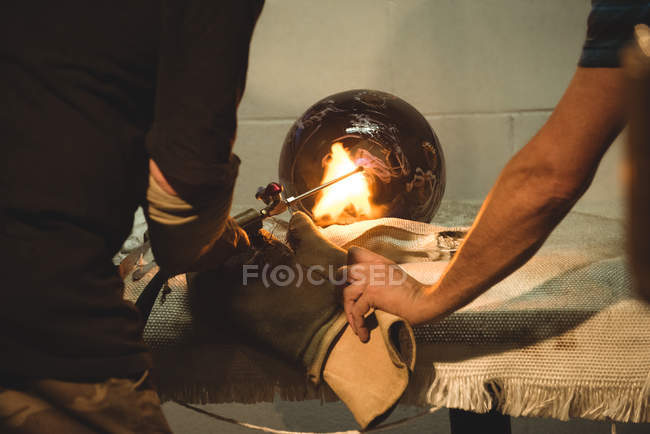 Equipe de sopradores de vidro soprando chama de gás propano em peça de vidro acabado na fábrica de sopro de vidro — Fotografia de Stock