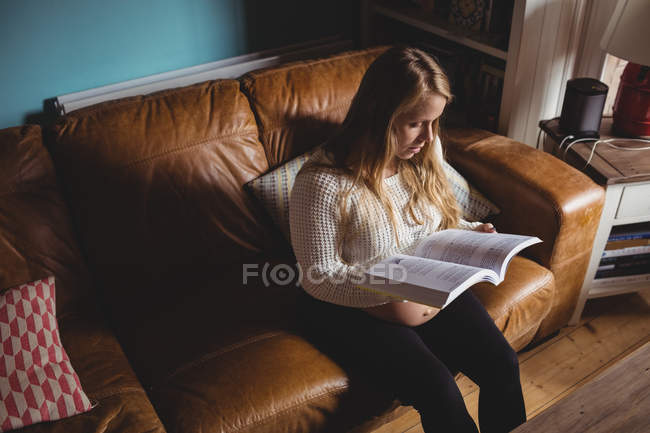 Pregnant woman reading book in living room at home — Stock Photo