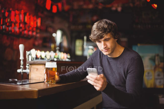 Чоловік використовує мобільний телефон зі склянкою пива в руці в барі — стокове фото