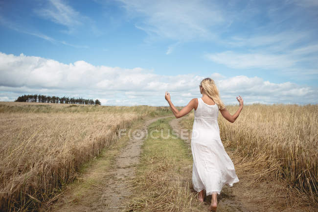 Rear view of blonde woman walking on path in field — Stock Photo
