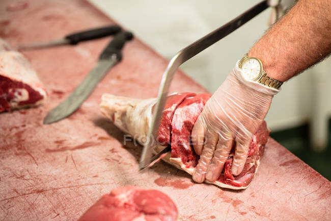 Manos de carnicero cortando canal de cerdo con una sierra en carnicería - foto de stock