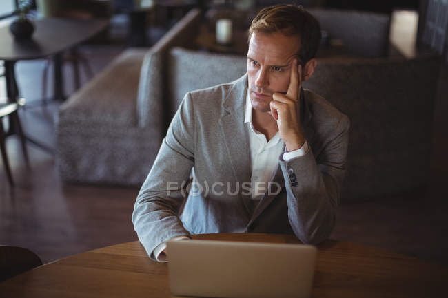 Pensativo hombre de negocios utilizando el ordenador portátil en el escritorio en la oficina - foto de stock