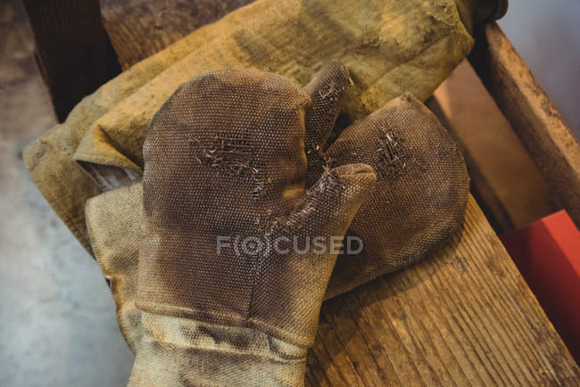 Primer plano de guantes de soplado de vidrio en la mesa en la fábrica de soplado de vidrio - foto de stock