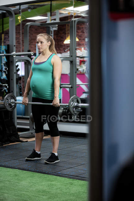 Pregnant woman working out with barbell at gym — Stock Photo