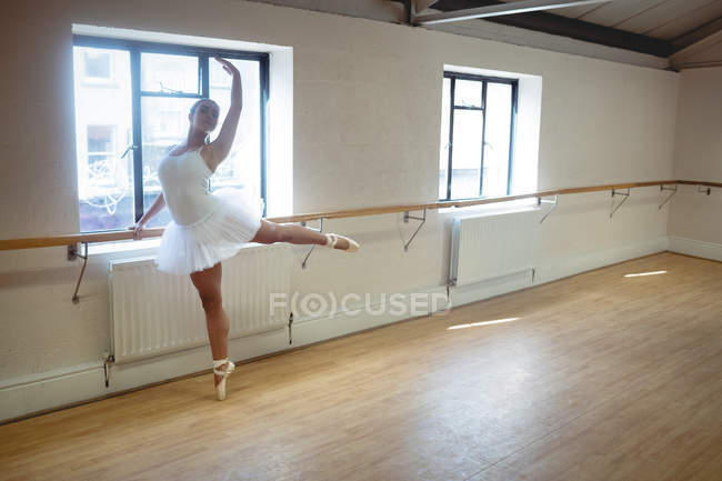 Ballerina che si allunga sulla sbarra mentre pratica la danza classica in studio — Foto stock