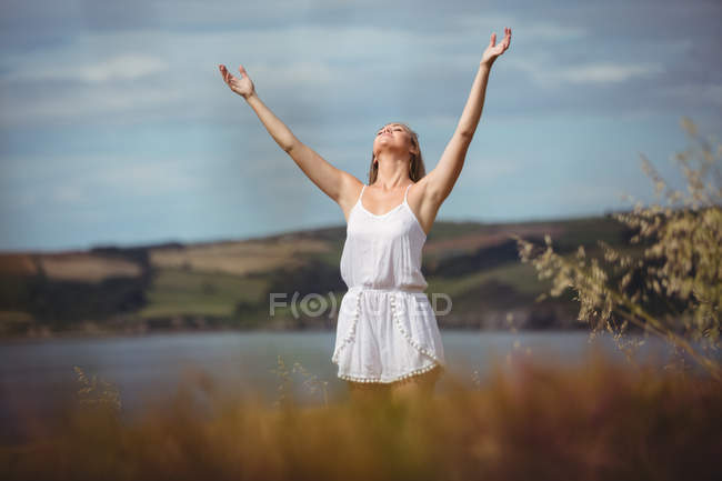 Donna in piedi in campo con le mani alzate e guardando in alto — Foto stock