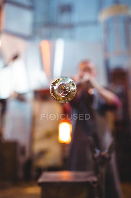 Soplador de vidrio dando forma a un vidrio en la tubería de soplado en la fábrica de soplado de vidrio - foto de stock
