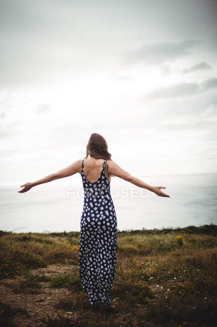 Rear view woman standing with outstretched arms on cliff near sea — Stock Photo