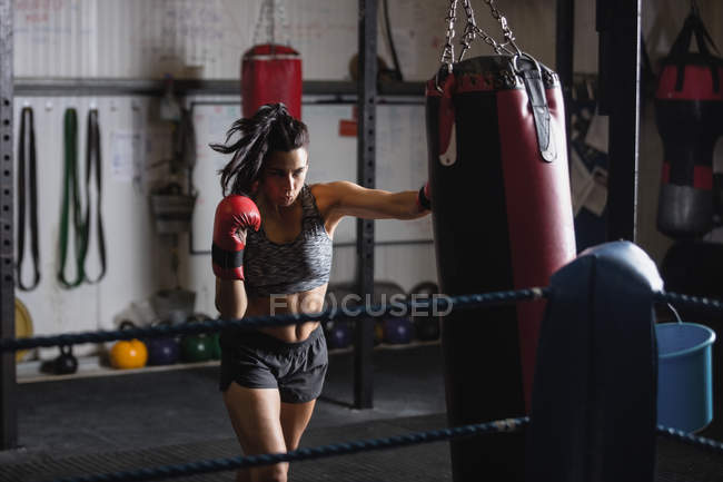 Fiduciosa pugile femminile pratica boxe con sacco da boxe in palestra — Foto stock