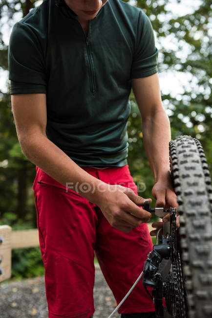 Male cyclist repairing his bicycle in forest on a sunny day — Stock Photo