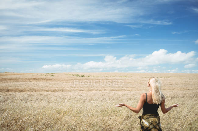 Вид сзади на блондинку, стоящую в поле с распростертыми объятиями — стоковое фото