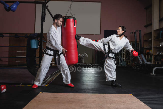Sportswoman and sportsman practicing karate with punching bag in studio — Stock Photo