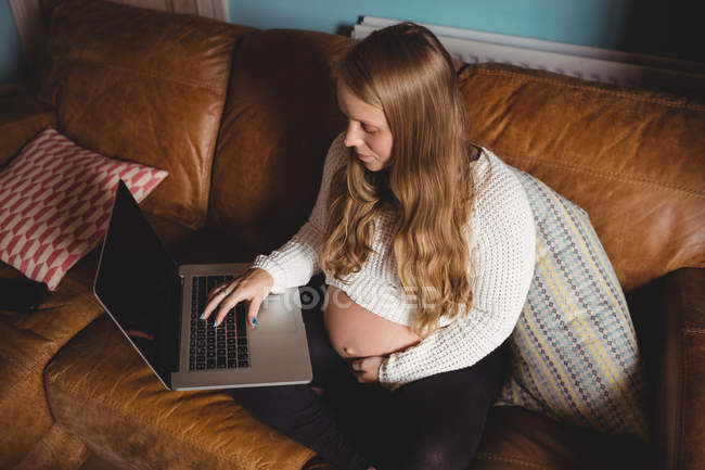 Vista ad alto angolo della donna incinta che utilizza il computer portatile in soggiorno a casa — Foto stock