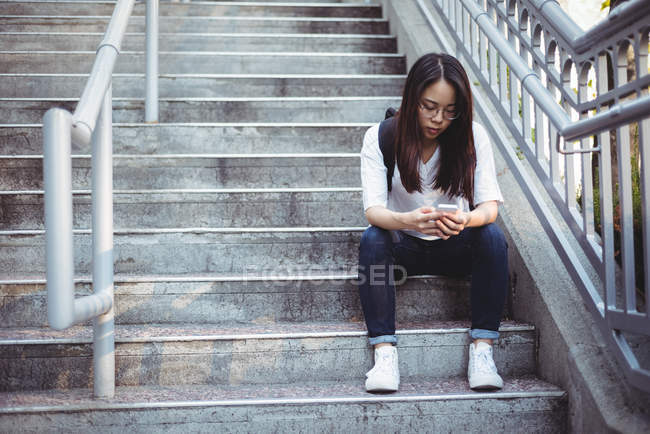 Young woman sitting on staircase and using mobile phone — Stock Photo