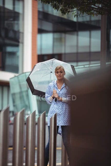 Enfoque selectivo de la hermosa mujer sosteniendo paraguas y apoyándose en el polo durante la temporada de lluvias - foto de stock