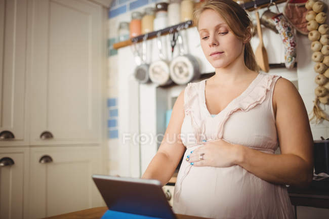 Schwangere nutzt digitales Tablet zu Hause in der Küche — Stockfoto