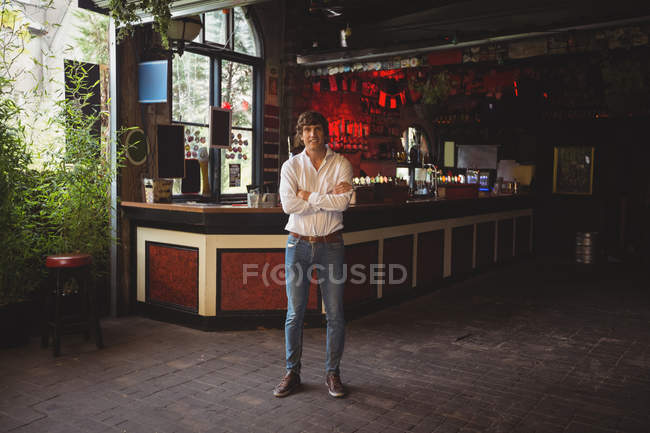 Portrait of smiling man standing with arms crossed in bar — Stock Photo