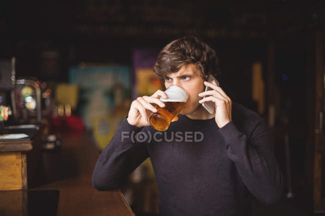 Человек разговаривает по мобильному телефону за бокалом пива в баре — стоковое фото