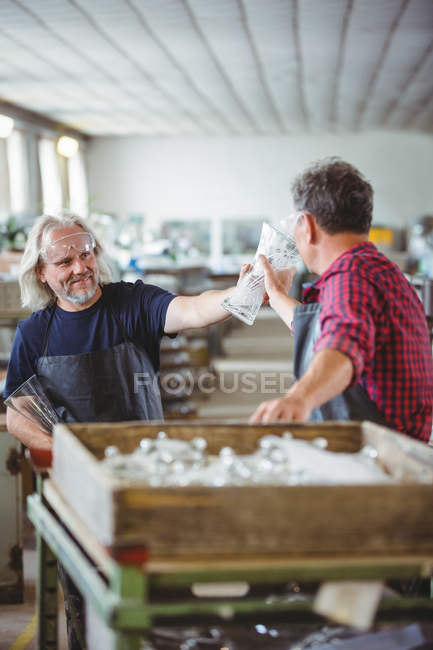 Soplador de vidrio mostrando jarrón de vidrio a un colega en la fábrica de soplado de vidrio - foto de stock