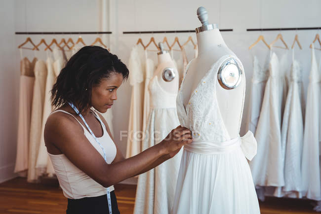 Diseñadora de moda femenina ajustando el vestido en un maniquí en el estudio - foto de stock