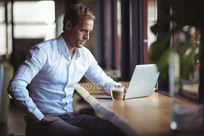 Selbstbewusster Geschäftsmann am Laptop mit Kaffee auf dem Tisch — Stockfoto