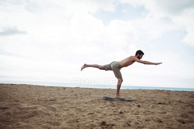 Человек, выполняющий упражнения на растяжку на пляже — стоковое фото