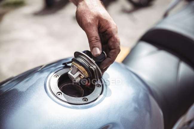 Mano del mecánico abriendo tanque de combustible de moto en taller - foto de stock