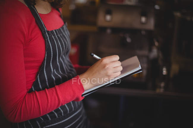 Mid-section of woman writing on diary in cafe at bicycle shop — Stock Photo