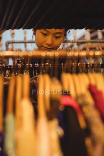 Jovem mulher selecionando roupas em cabides na loja de roupas — Fotografia de Stock