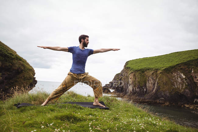Uomo che esegue esercizio di stretching sulla scogliera — Foto stock