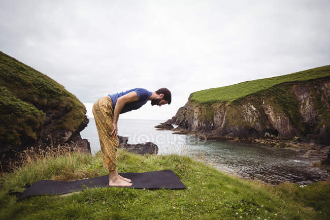 Hombre realizando yoga en acantilado - foto de stock