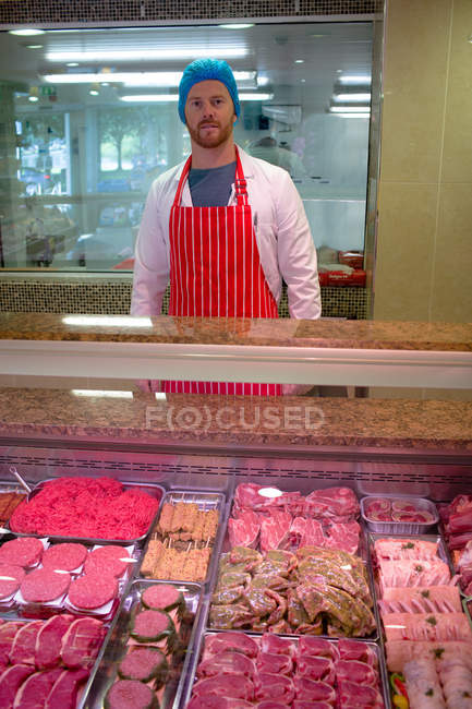 Retrato del carnicero parado en el mostrador de carne en la carnicería - foto de stock