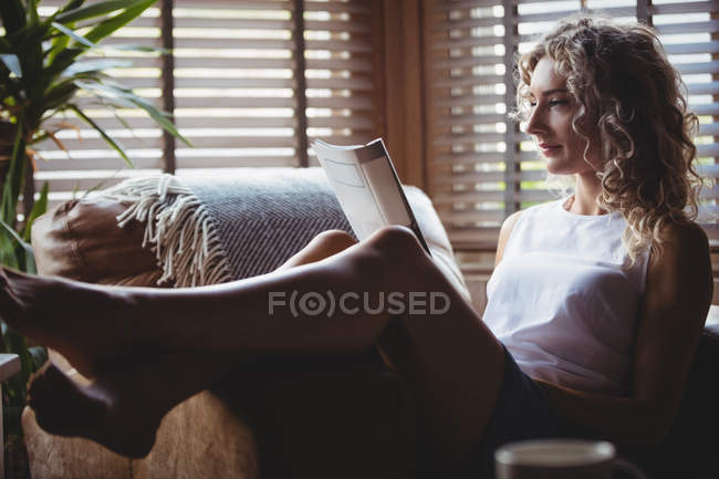 Schöne Frau liest Magazin im Wohnzimmer zu Hause — Stockfoto