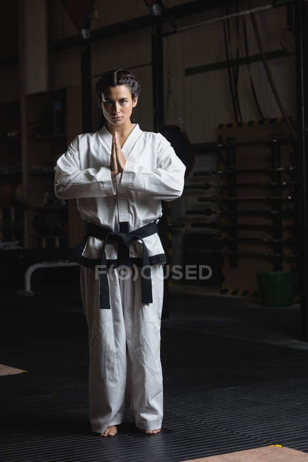 Portrait of woman in karate kimono standing with hands in namaste gesture in fitness studio — Stock Photo