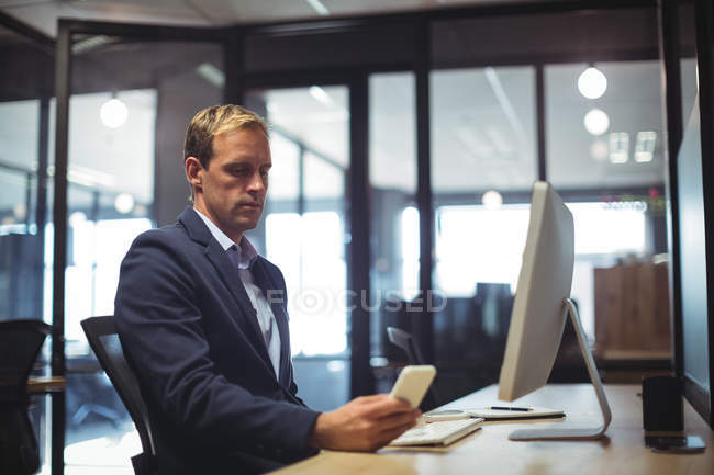 Geschäftsmann benutzt Handy während er am Schreibtisch im Büro sitzt — Stockfoto