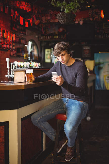 Чоловік використовує мобільний телефон зі склянкою пива в руці в барі — стокове фото