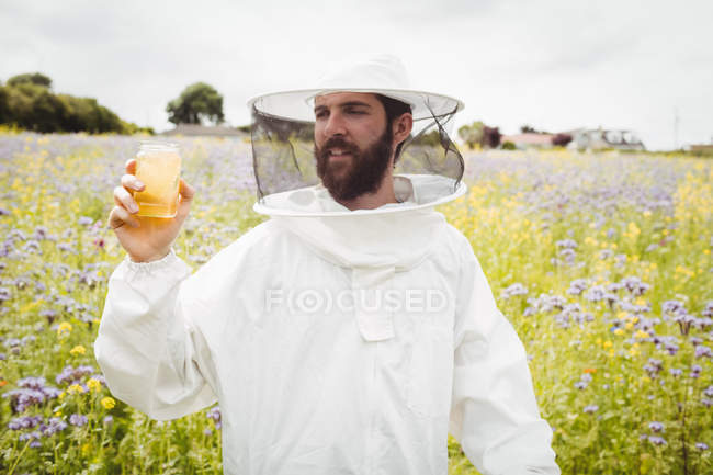 Apicultor sosteniendo botella de miel en el campo - foto de stock