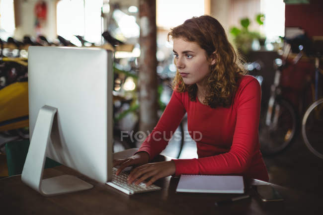 Mujer sentada en la mesa y usando la computadora en la tienda de bicicletas - foto de stock