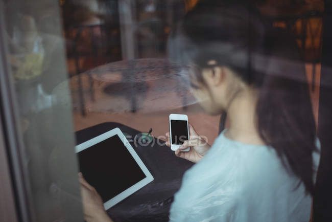 Вид ззаду жінки за допомогою мобільного телефону та цифрового планшета в кафе — стокове фото