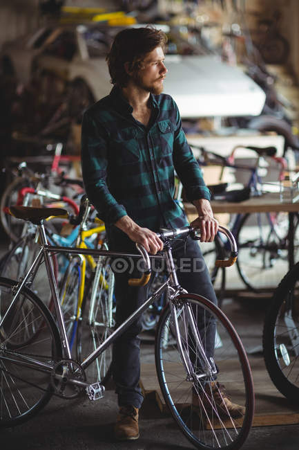 Thoughtful mechanic standing with bicycle in bicycle shop — Stock Photo