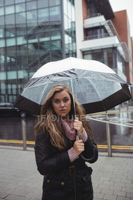 Portrait of beautiful woman holding umbrella during rainy season on street — Stock Photo