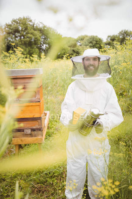 Portrait of beekeeper holding bee smoker in field — Stock Photo