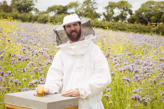 Apicoltore che tiene bottiglia di miele su alveare in campo — Foto stock