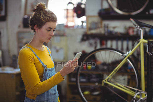 Механік, що використовує мобільний телефон у велосипедному магазині — стокове фото