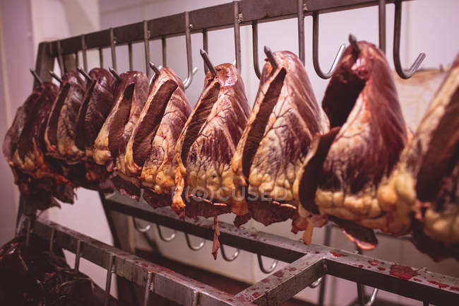 Corações de carne de vaca pendurados em uma fileira na sala de armazenamento no açougue — Fotografia de Stock