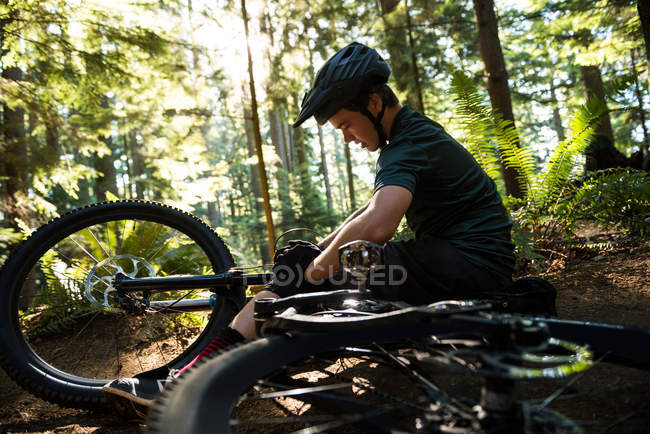 Ciclista masculino reparando su bicicleta en el bosque en un día soleado - foto de stock