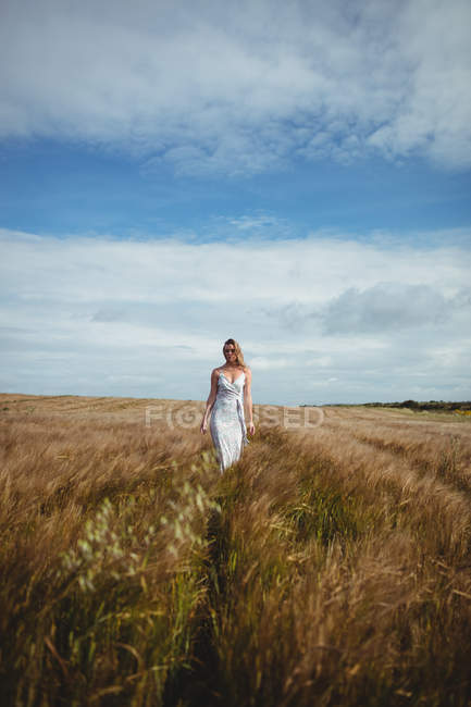 Beautiful woman walking through wheat field on sunny day — Stock Photo