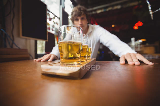 Bartender standing near counter with glasses of beer in bar — Stock Photo